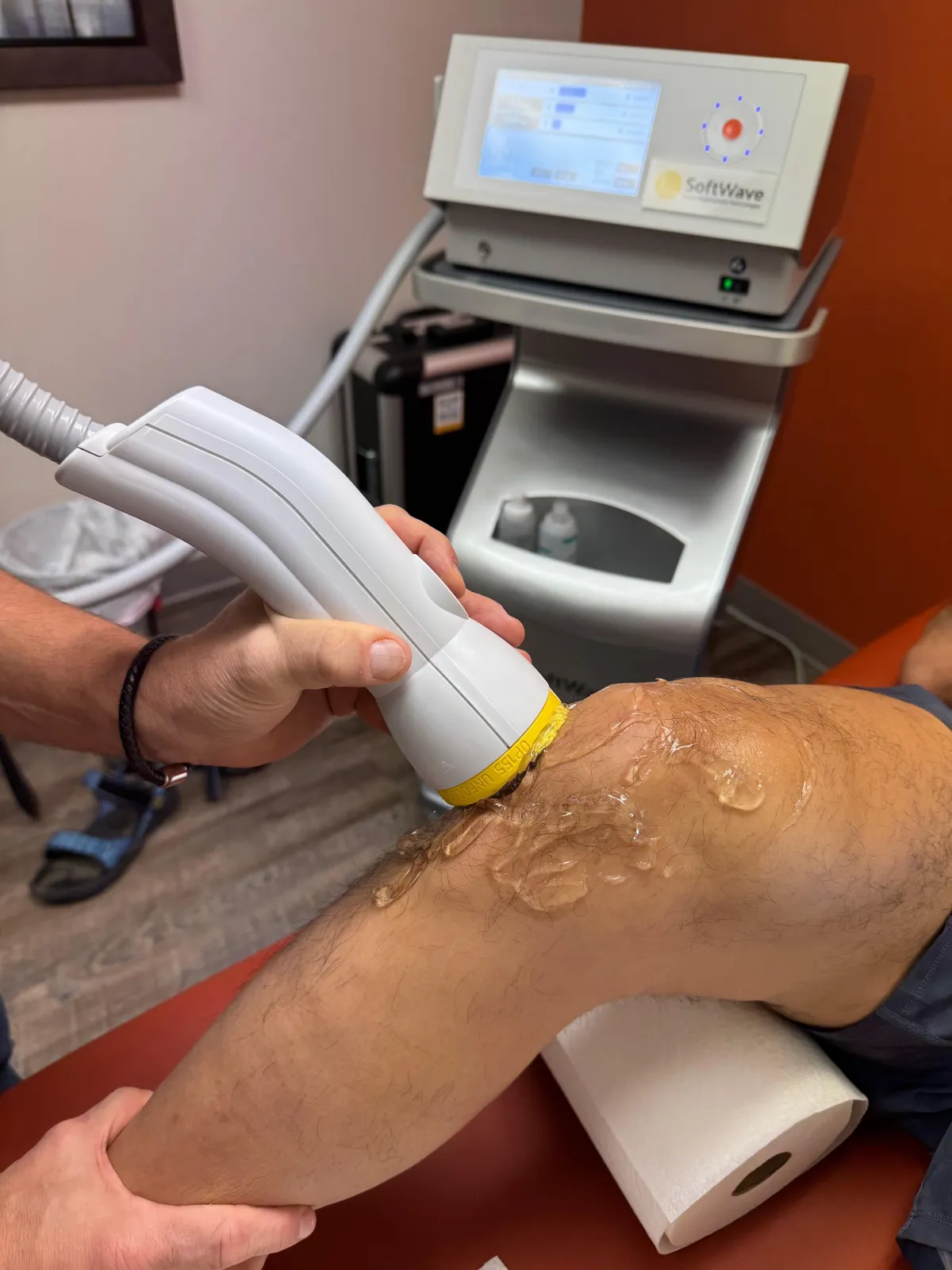 Medical professional applying a SoftWave therapy wand to a patient's knee in a clinical setting
