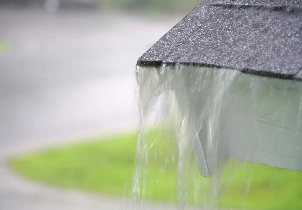 Close up on rain flowing from an old roof showing signs of storm damage