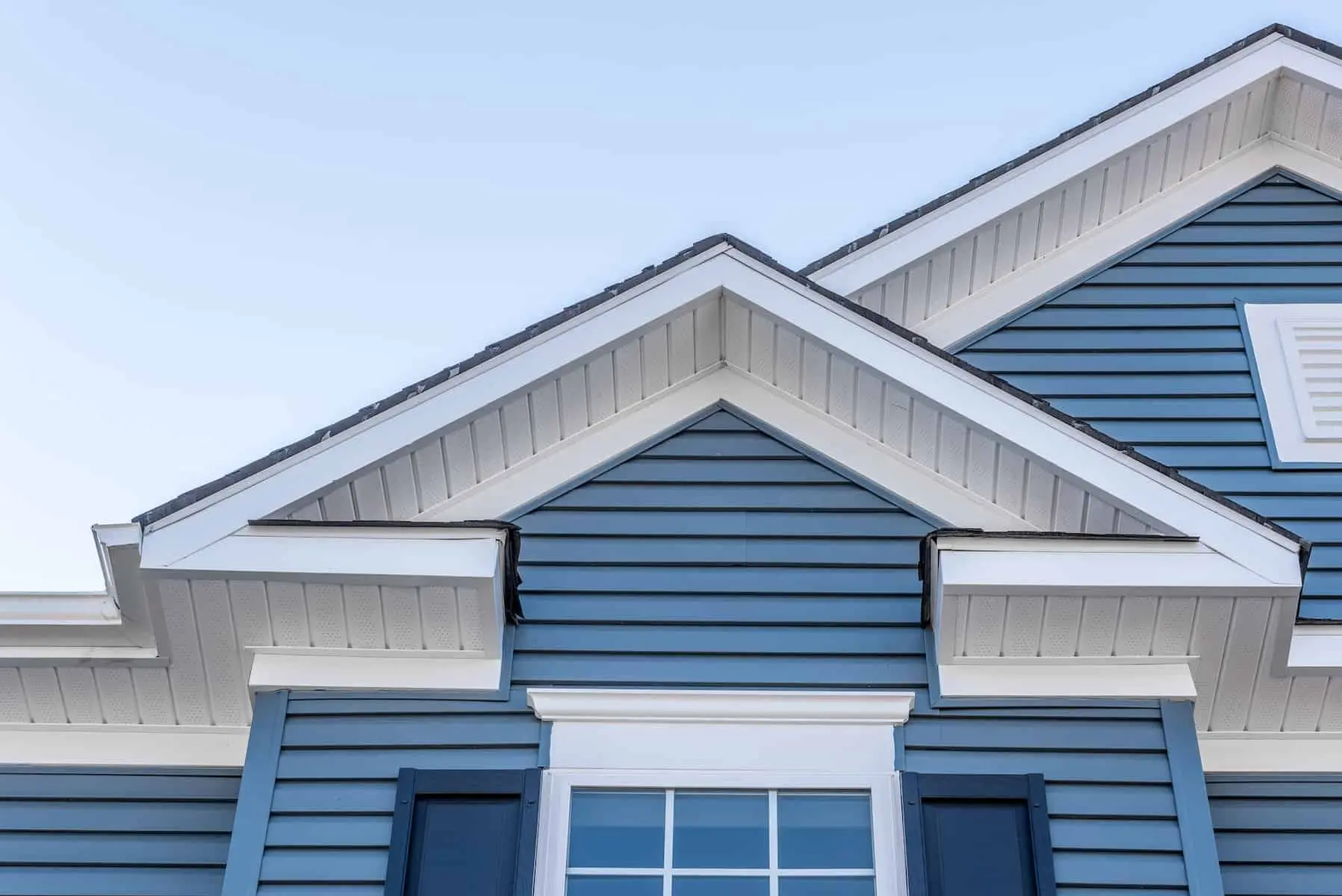 Decorative gable roof with white cornice, blue horizontal vinyl siding with light blue sky