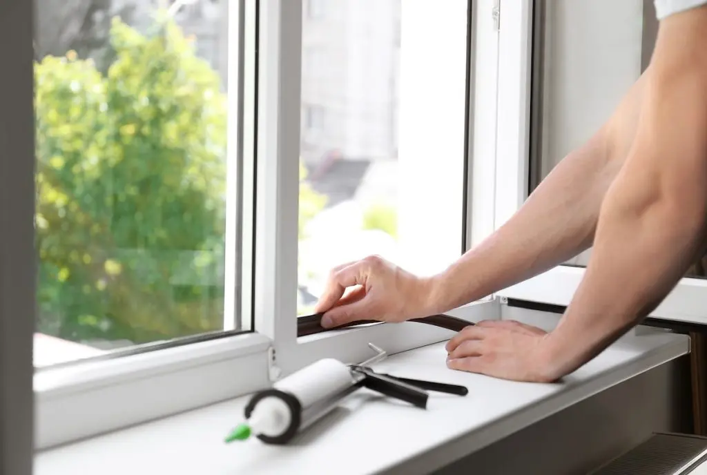window repair cost Construction worker putting sealing foam tape on window indoors