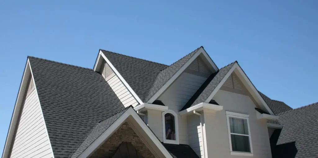 house with multiple gabled roofs, gray shingles, and light-colored siding against a clear blue sky