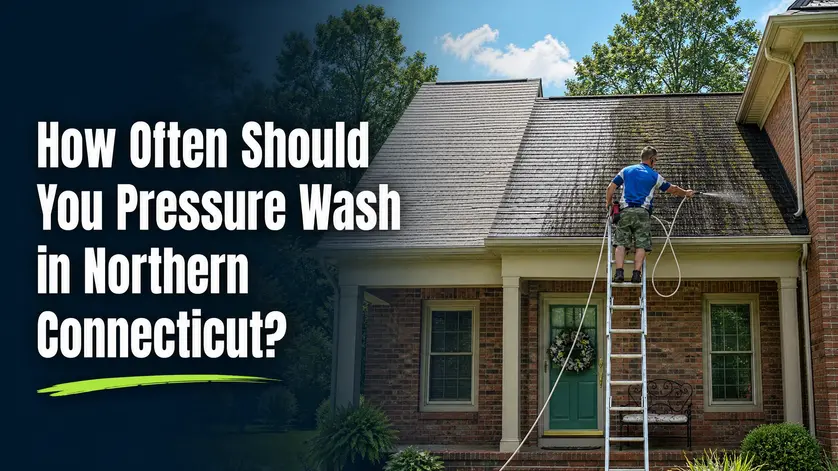 Soft wash technician on a ladder cleaning an algae-covered roof on a Northern Connecticut home, with the blog title How Often Should You Pressure Wash in Northern Connecticut overlaid on the left side