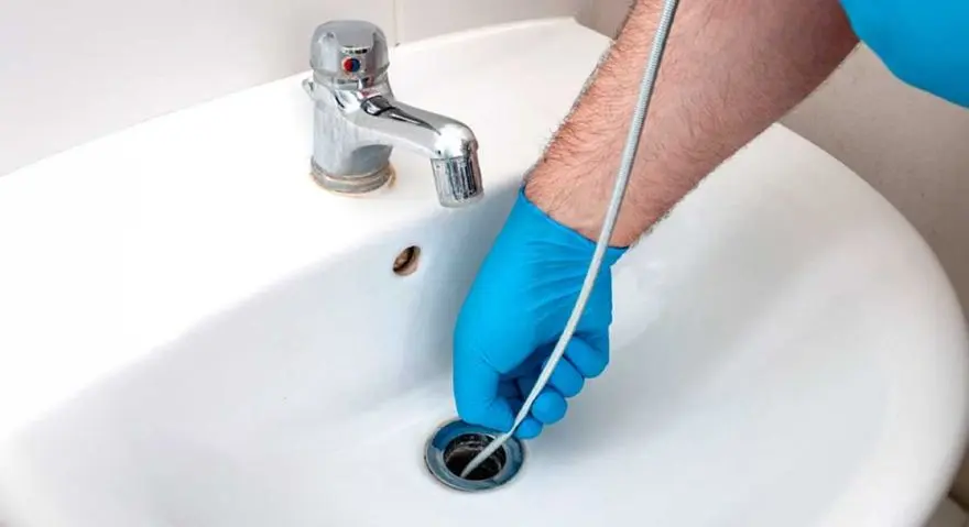 Plumber using a drain snake in a white sink