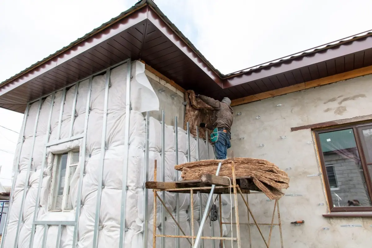 The worker insulates the walls of the house from the outside. Preparation for the installation of saiing.