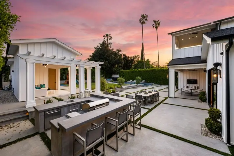 the outdoor kitchen with a fireplace table and chairs at dusk | Search Strategy Marketing the outdoor kitchen with a fireplace table built by landscapers at dusk