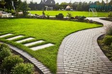 Landscaping of the garden path curving through Lawn with green grass and walkway tiles