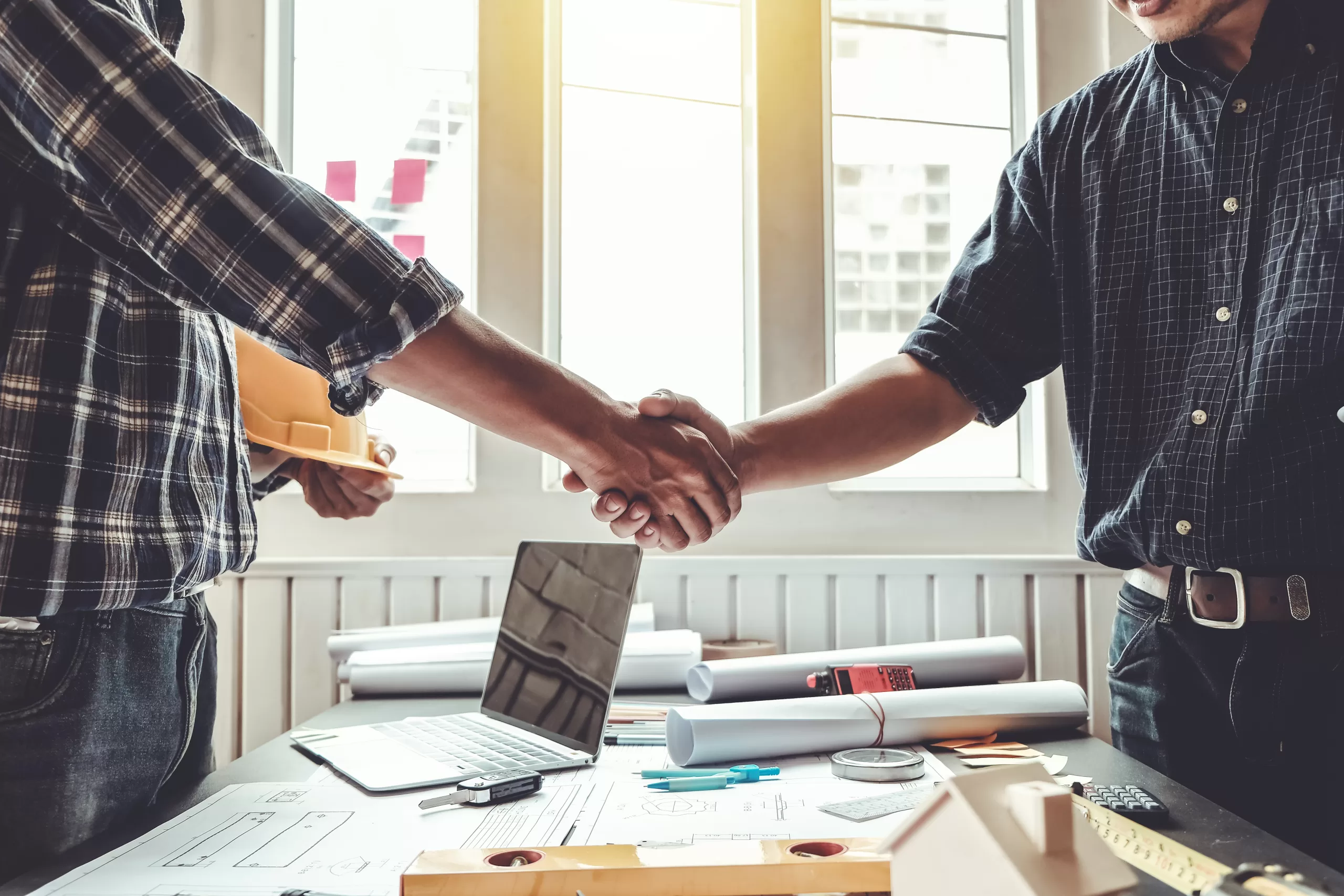 Engineer and contractor shaking hands success of the project wor | Search Strategy Marketing a contractor and a marketing agency owner shaking hands over a desk and a laptop