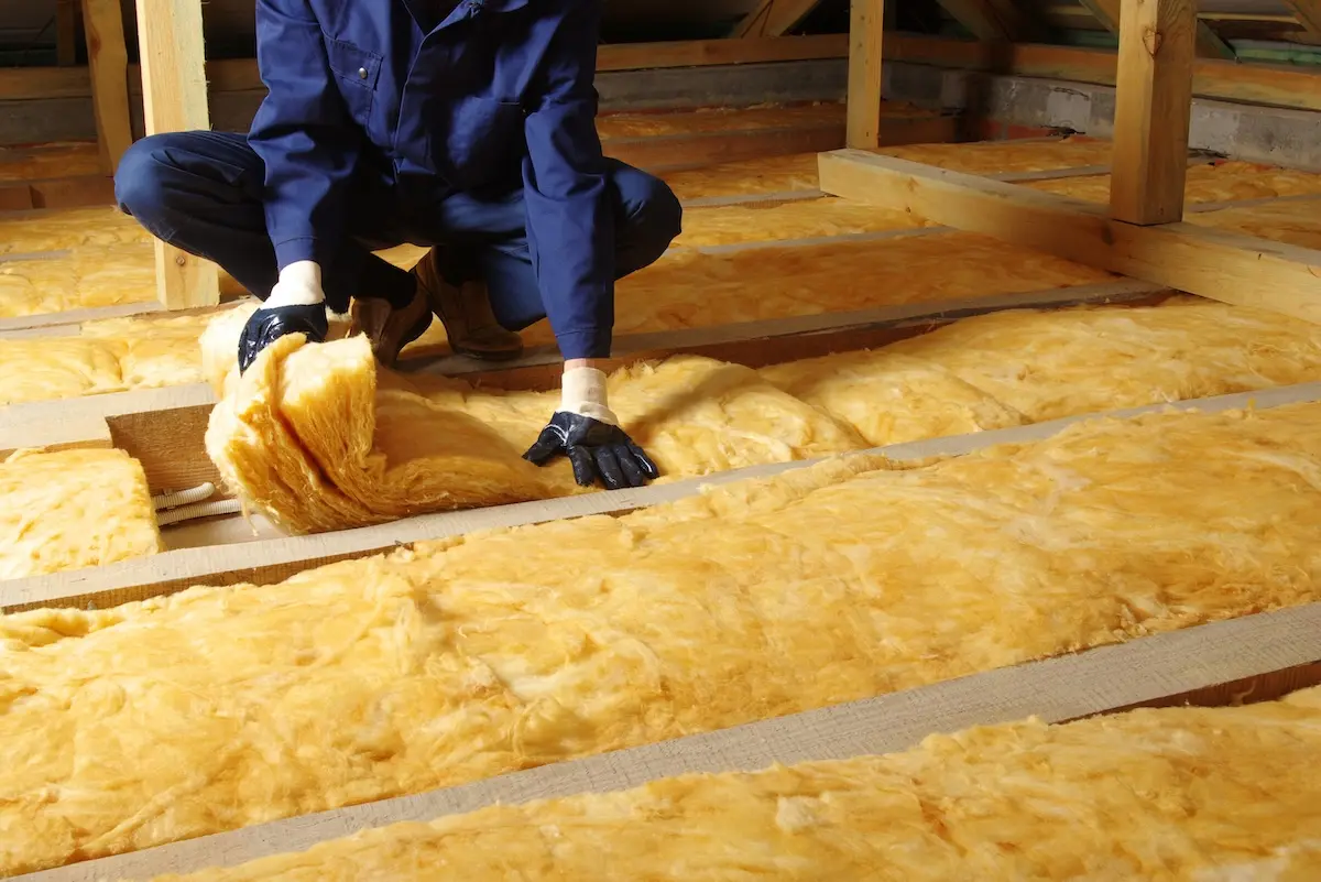 Man installing thermal insulation layer under the roof, using mineral glass wool