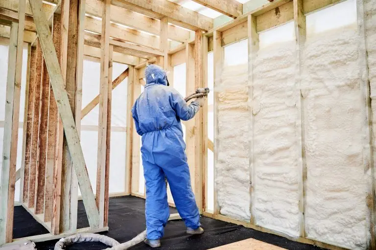 Worker spraying polyurethane foam insulation into timber wall cavities