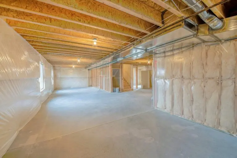 Large unfinished basement with woodframes and wall insulation. Basement interior with plastic vapor barrier and windows on the left side.