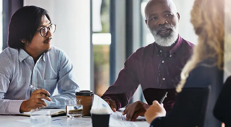 Three individuals engaged in a discussion while seated at a table during a meeting