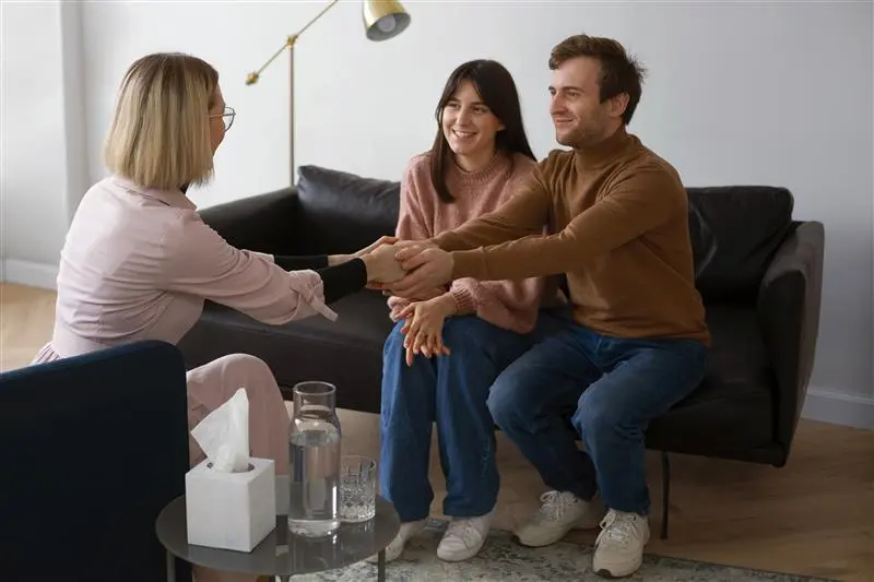 a couple sitting on a couch shakes hands, symbolizing agreement or connection between them