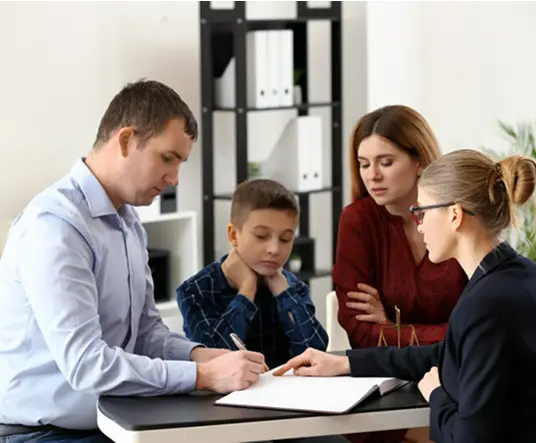 A family sits with an advisor at a table, reviewing documents. The scene appears focused and serious, highlighting cooperation and decision-making.