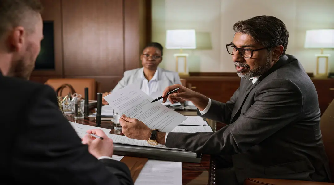 Mature male boss or chief executive officer with paper document in hands looking at younger colleague during explanation of contract points