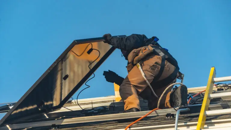 worker holding solar panel on top of a roof