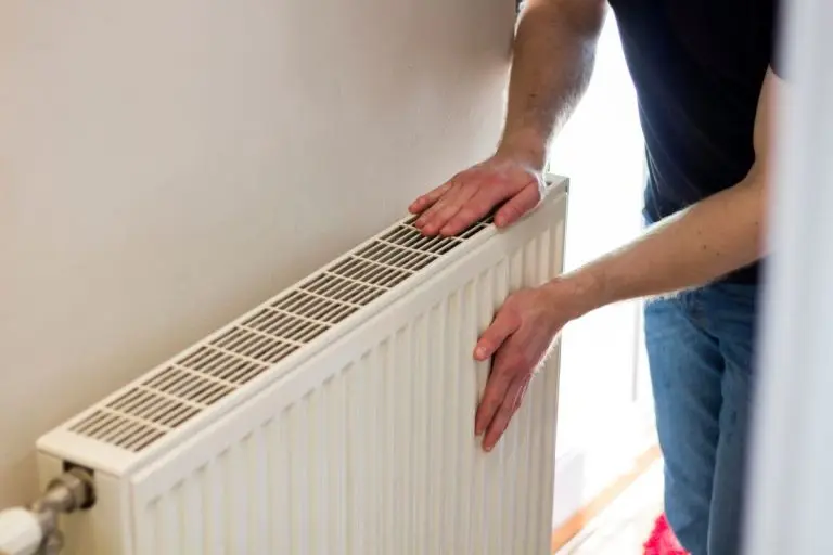 Man is checking radiator is it heating. Man warming his hands on the radiator. Home central heating system.