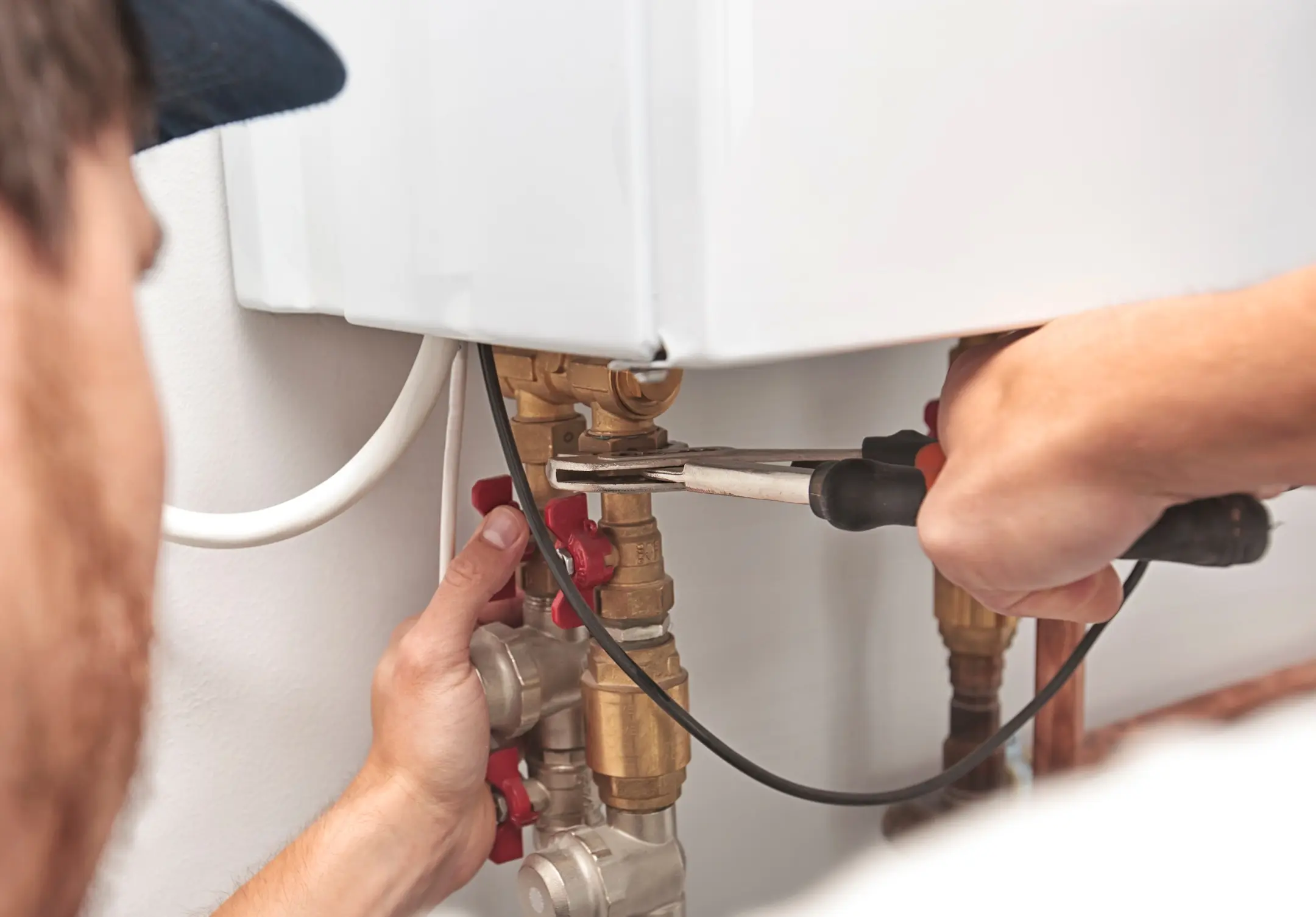 The man is installing the heater system in the house and checking pipes by the wrench