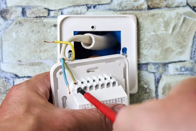 Connecting wires to wall thermostat for floor heating system, an electrician uses crosshead screwdriver for installation.