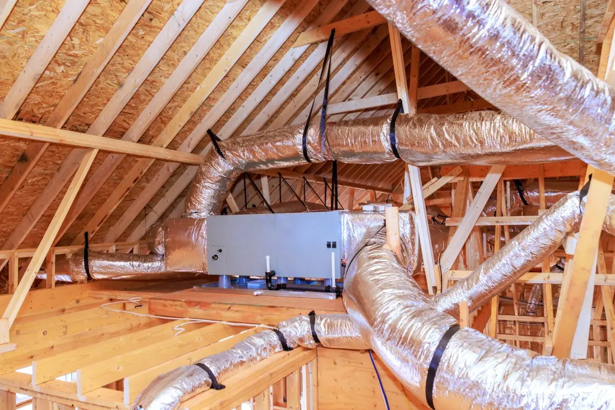 Workers install ducting ventilation systems in attic space of house under construction.