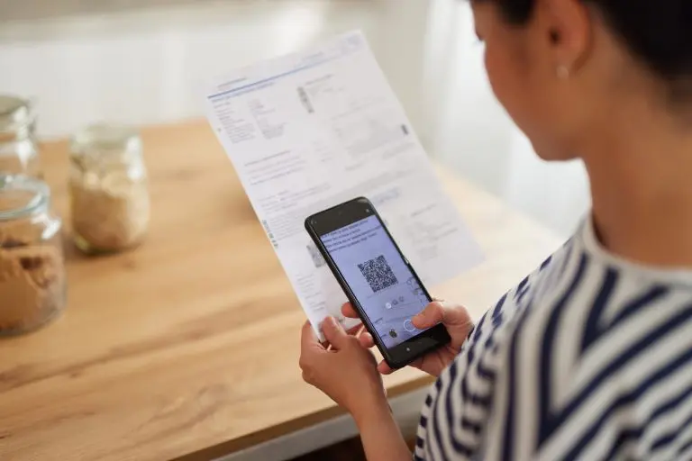 woman standing in the kitchen with mobile phone paying bills online