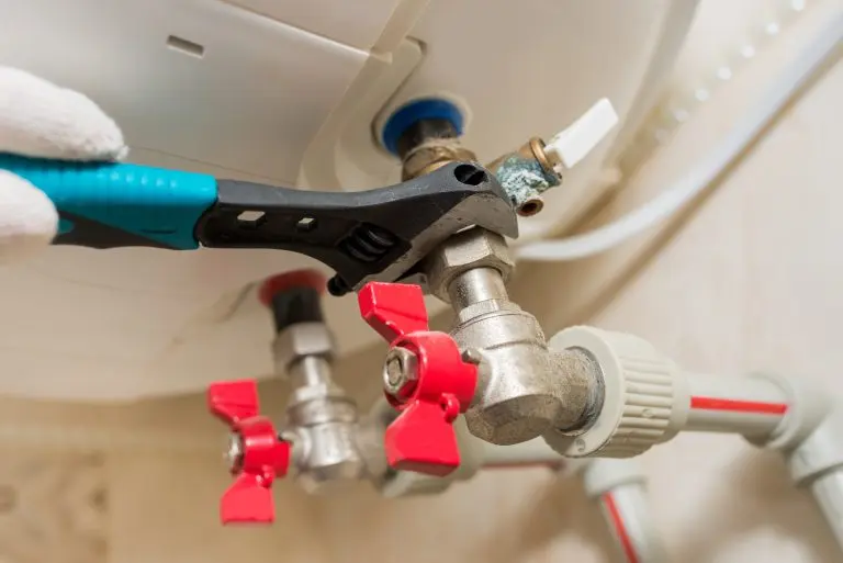 A worker in a nut on a boiler water heater with a plumbing wrench