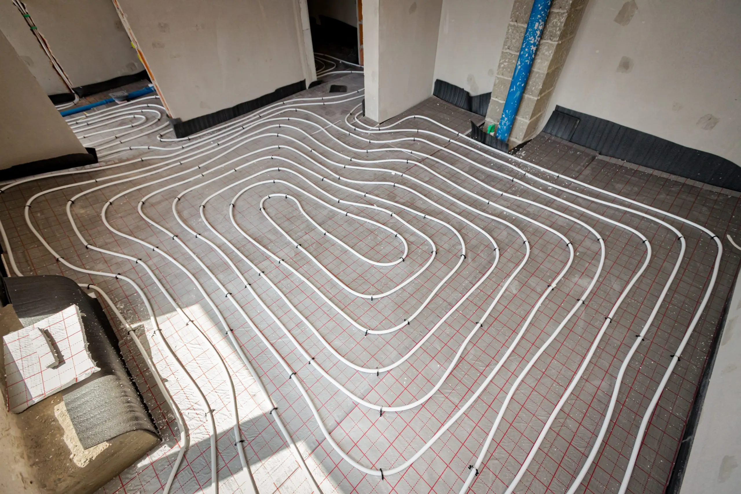 View on thin white tubes bended in complex curve of new brass, distribution system manifold mounted for central heating floor in a residential building under construction.