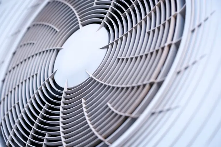 Fascinating abstract geometric pattern created by the circular gray plastic ventilation grille covering the rotating fan blades of a modern outdoor air conditioning unit