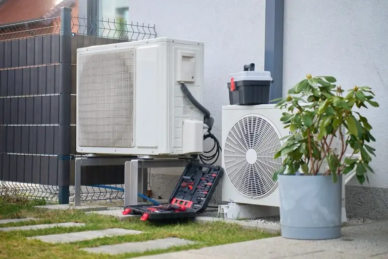 Outdoor heat pump units beside house with open toolbox and tools on ground.
