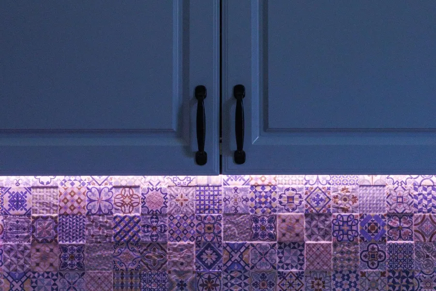blue kitchen cabinets with a patterned decorative tile backsplash and under cabinet lighting