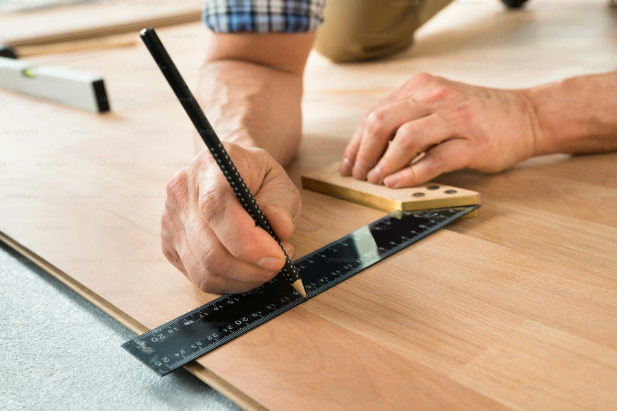 Close-up of a worker drawing a mark on laminate using ruler.