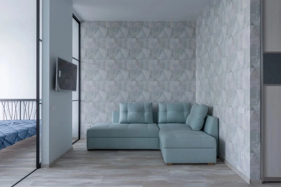 Comfortable sofa with cushions placed near wall with wallpaper.