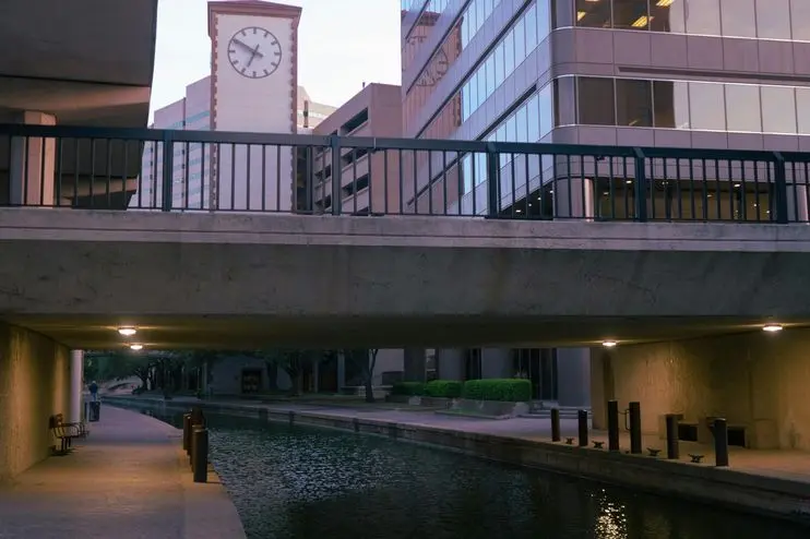 Scenic view of canal under modern bridge with clock tower and buildings in Irving, TX.