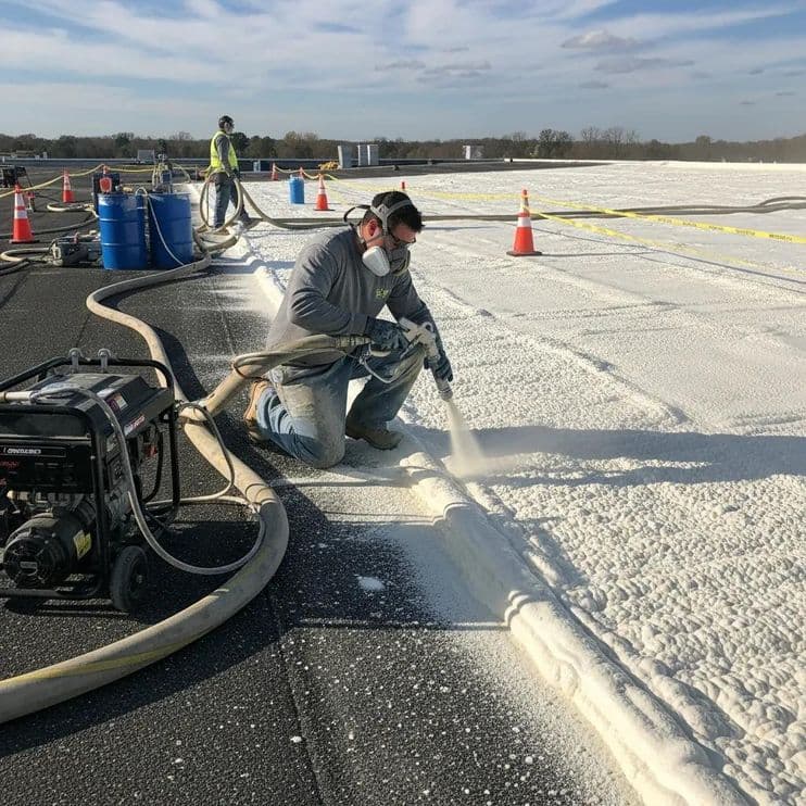 Contractor applying spray foam insulation during roofing installation on a commercial building, showcasing the application process and equipment used for enhanced durability and weather resistance.
