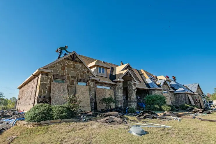 Brick house in Weatherford, Texas undergoing roof installation. Workers on roof under clear sky.
