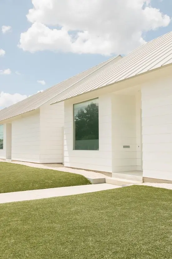 A modern white house in Houston with large glass windows and a sleek design, under a clear blue sky.