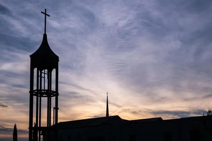 Silhouetted church tower with cross against a sunset sky in Plano, Texas.