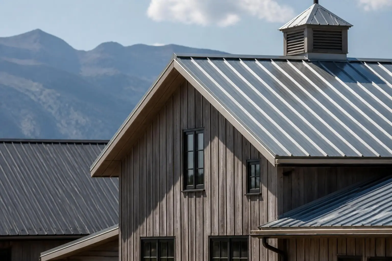 Metal roofing installation on a modern barn-style home and building, showcasing durable tin roofing benefits.