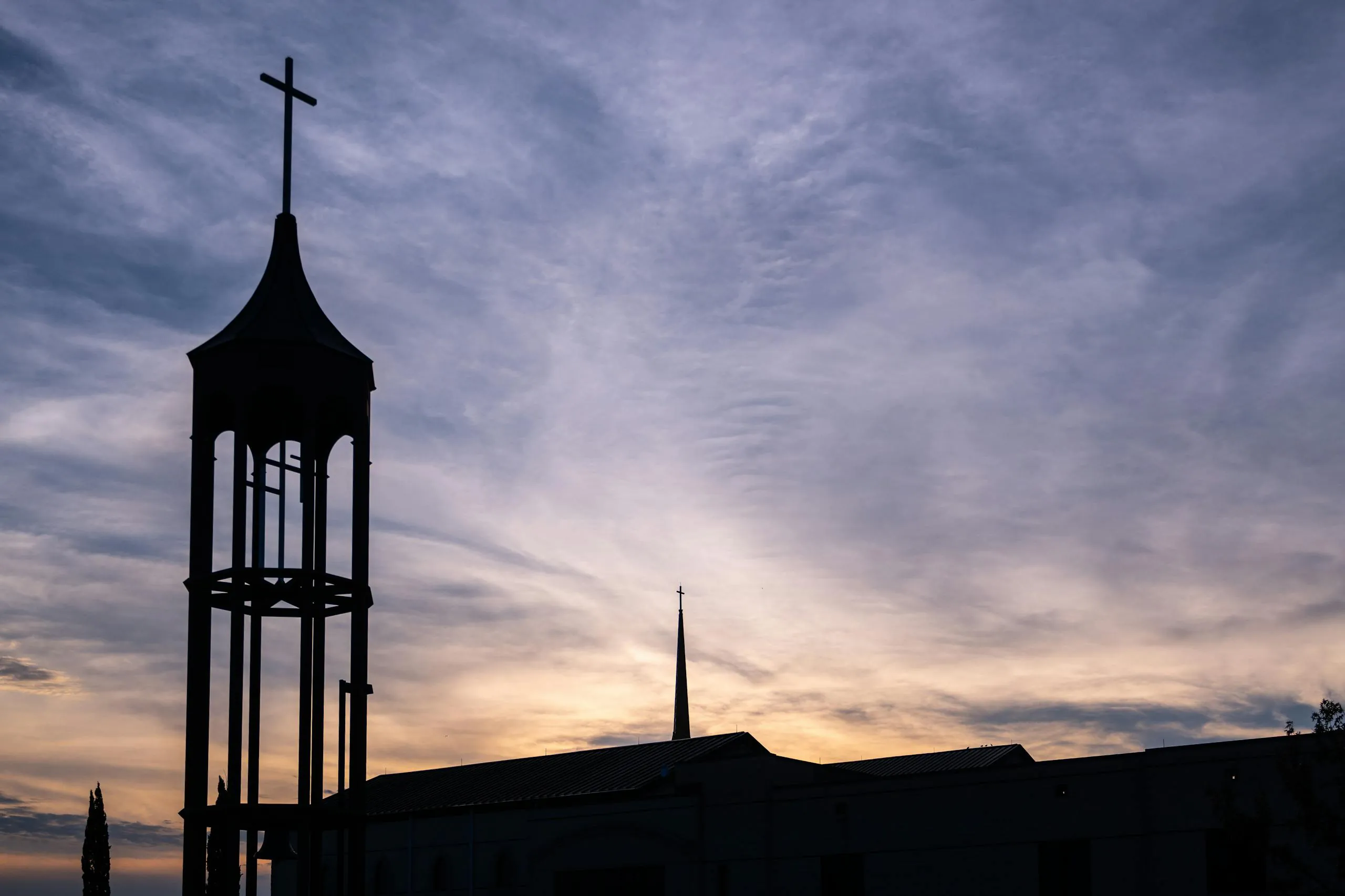 Silhouetted church tower with cross against a sunset sky in Plano, Texas.