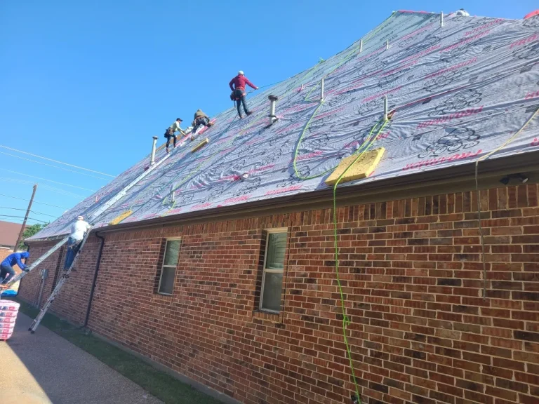 Roofers installing new underlayment on a large brick house roof.