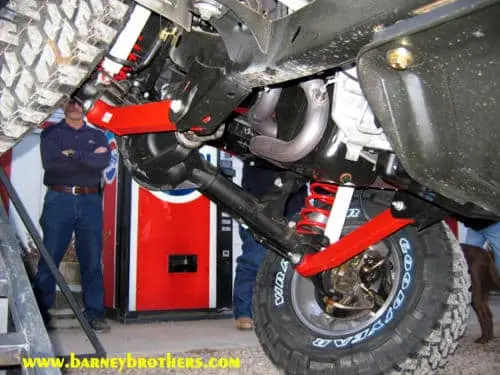Close-up view of a vehicle's red and black suspension with an off-road tire in front of a Pepsi vending machine.
