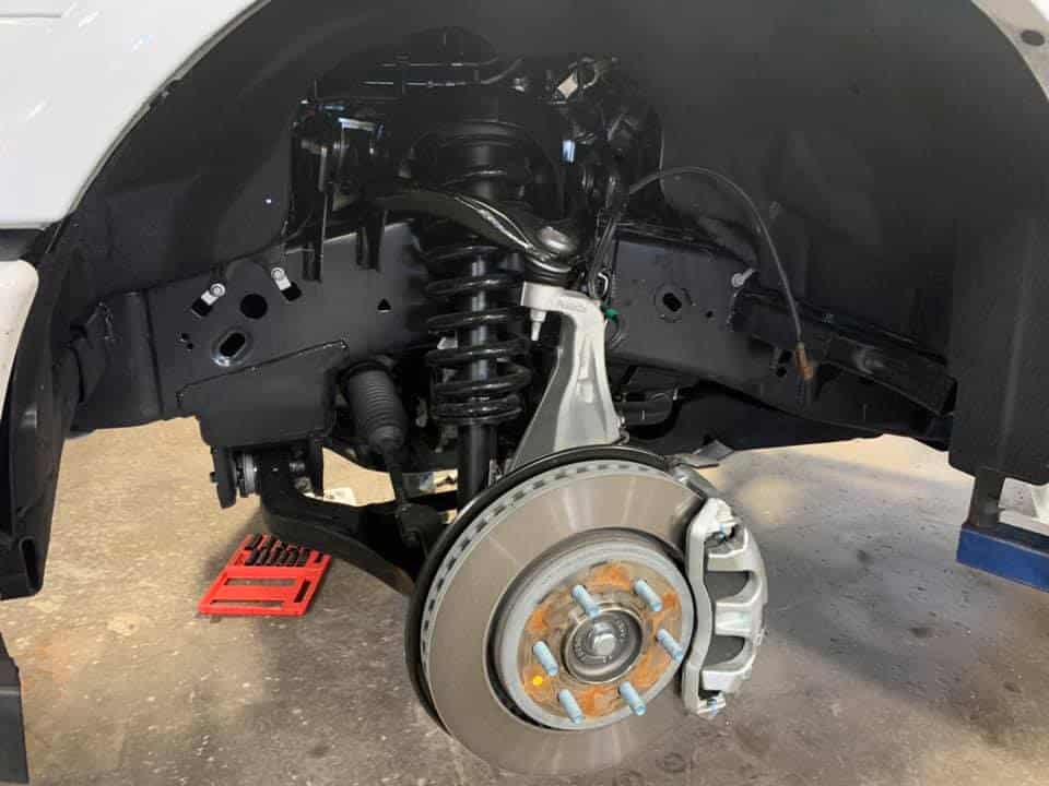 A close-up of a car's front suspension system with the wheel removed, showcasing the brake disc and coil spring—a vital view for anyone considering brake repair.