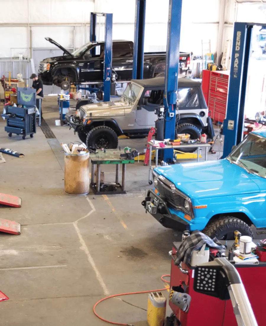 Auto repair shop with vehicles on lifts, including a black truck, silver SUV, and blue SUV. Auto repair mechanics are working nearby.