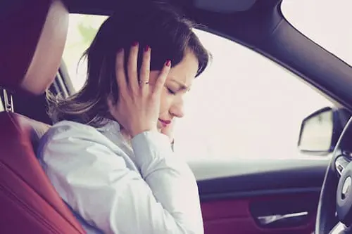 Woman inside a car with her hands covering her ears, looking distressed by the overwhelming car noises.