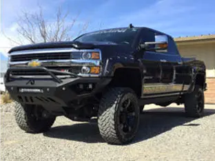 A black lifted Chevrolet pickup truck, one of our impressive customer rigs, is parked on a gravel driveway with a building and tree in the background.