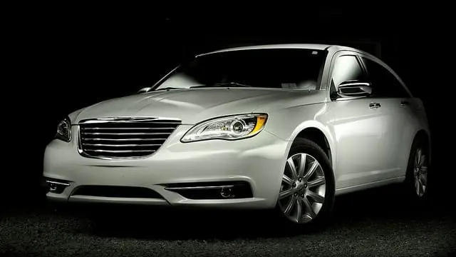 A Chrysler white sedan car illuminated against a dark background, showcasing its front and side view.