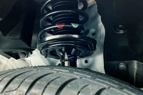 Close-up of a car's suspension system with a coil spring and a tire in the foreground, showcasing the intricacies of modern engineering.