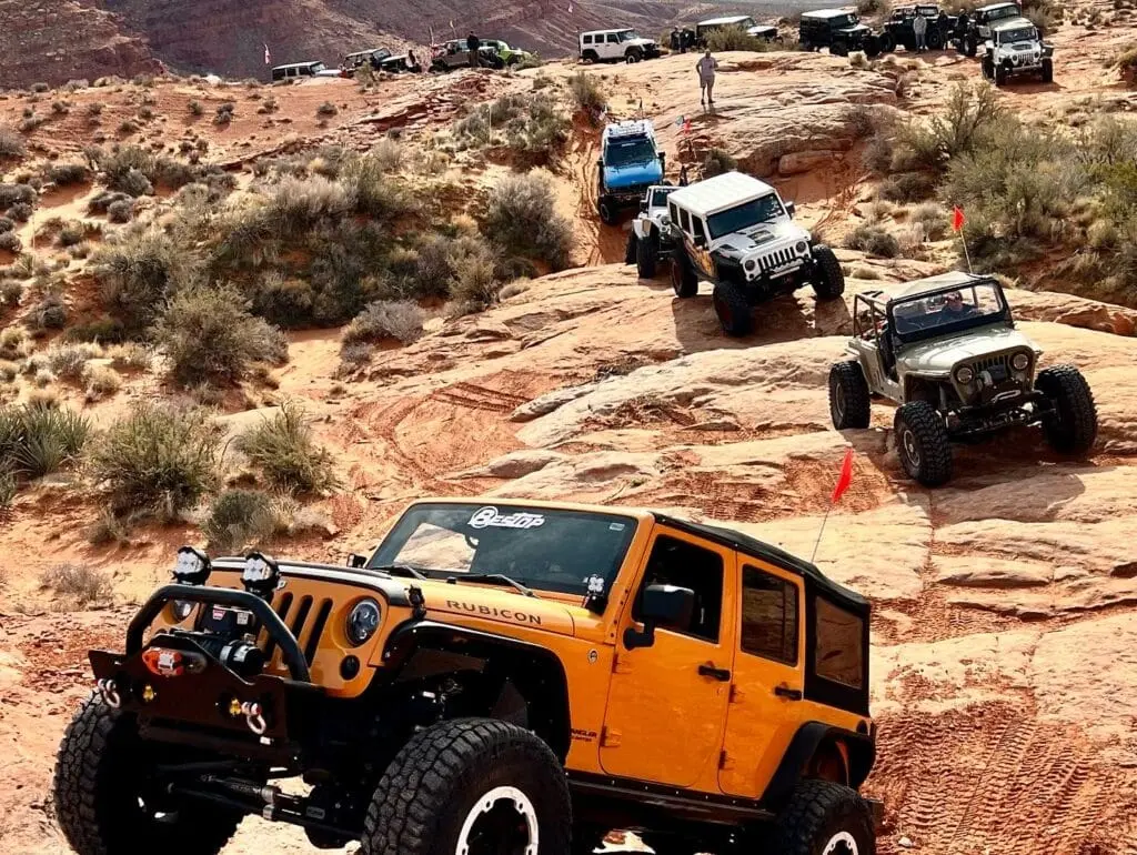 A group of 4 x 4 vehicles driving over rugged, rocky terrain with a mountainous landscape in the background, ideal for off-roading enthusiasts.