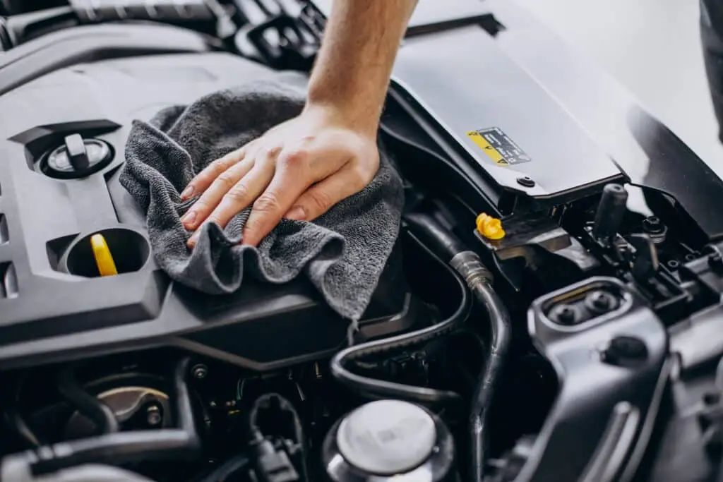 A hand meticulously cleaning a car engine with a gray cloth, ensuring every detail shines, as part of a major service.