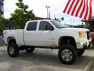 A white lifted pickup truck, one of our standout customer rigs, proudly parked beside an American flag.