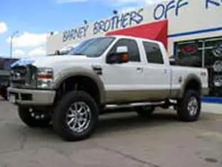 A lifted white pick-up truck, one of the impressive customer rigs, is parked outside a shop with "Brothers Off-Road" signage.